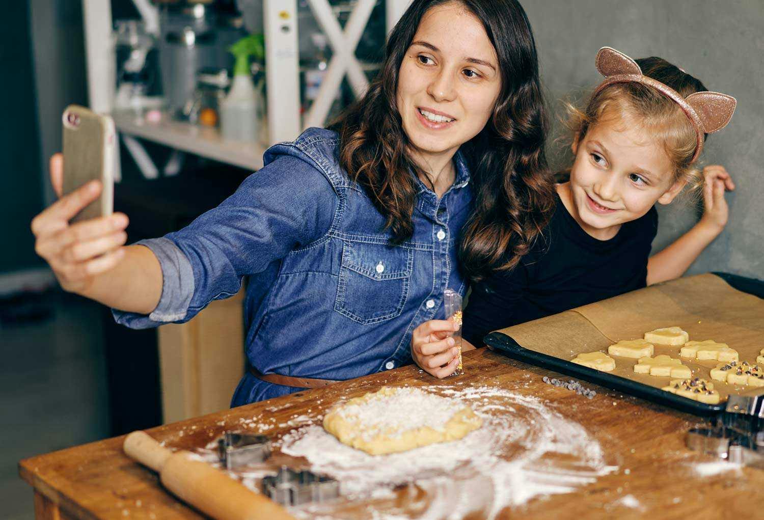 A mother taking a selfie while decorating cookies with her daughter