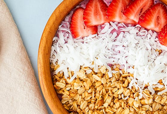 A bowl of strawberries, coconut and grains.