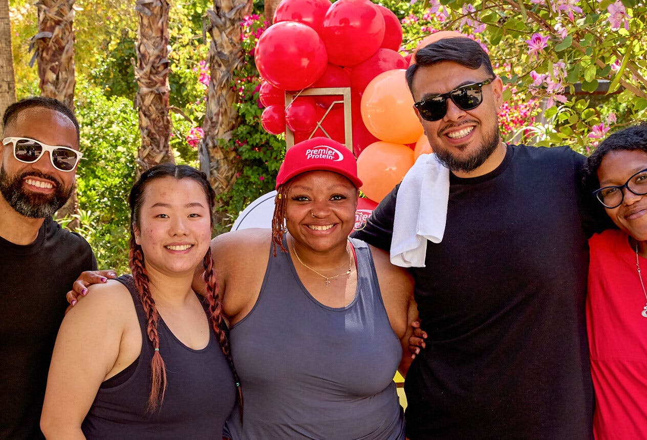 Five Premier shakers wearing Premier Protein gear pose in front of red balloons.