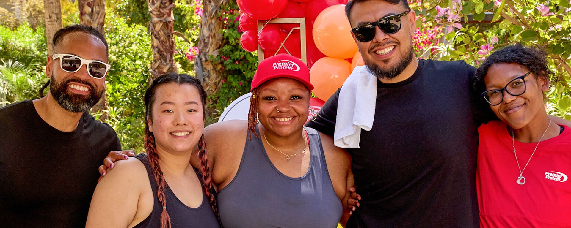 Five Premier shakers wearing Premier Protein gear pose in front of red balloons.