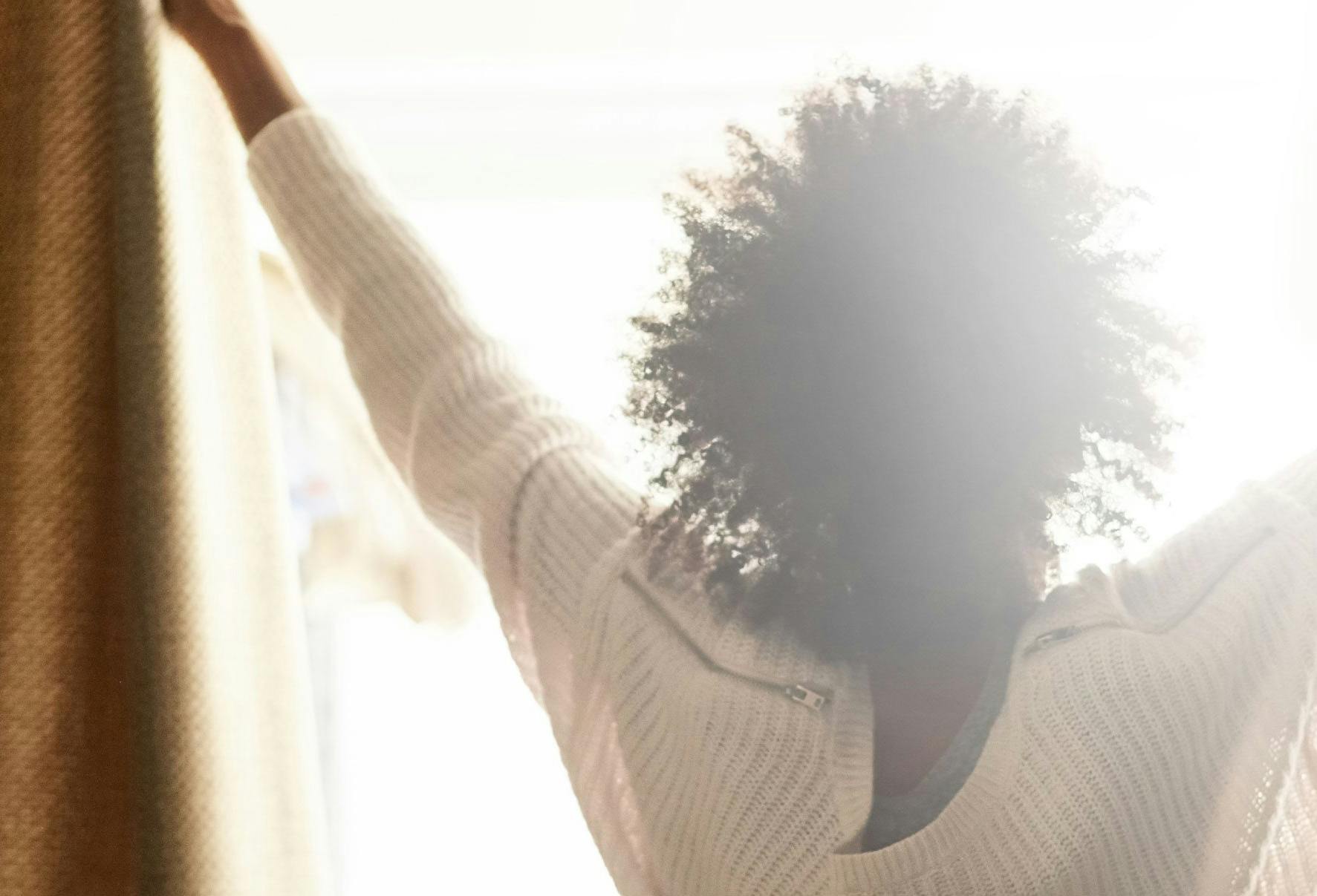 A women opening her curtain to let the sun shine into her room.