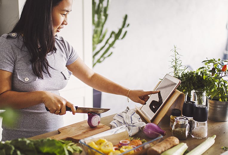 A woman chopping vegetables in her kitchen.