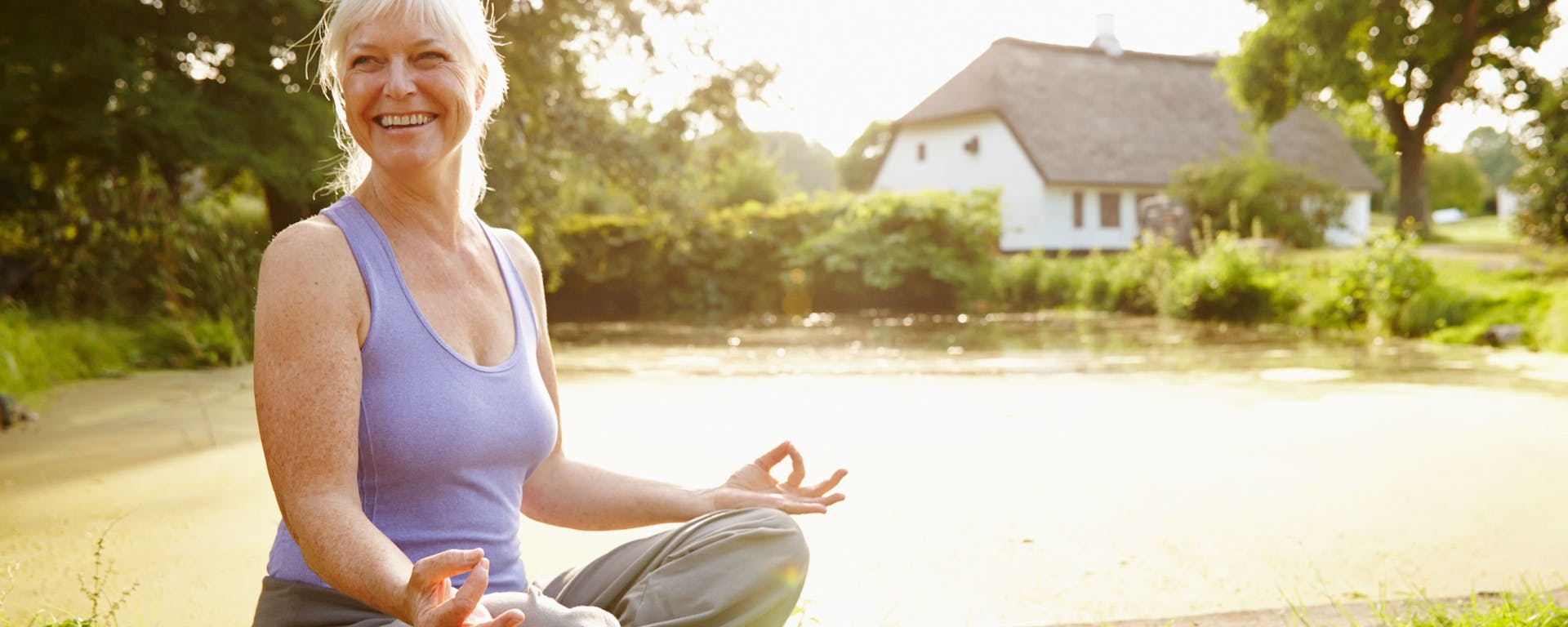 A woman meditating in the sunshine next to a small pond.