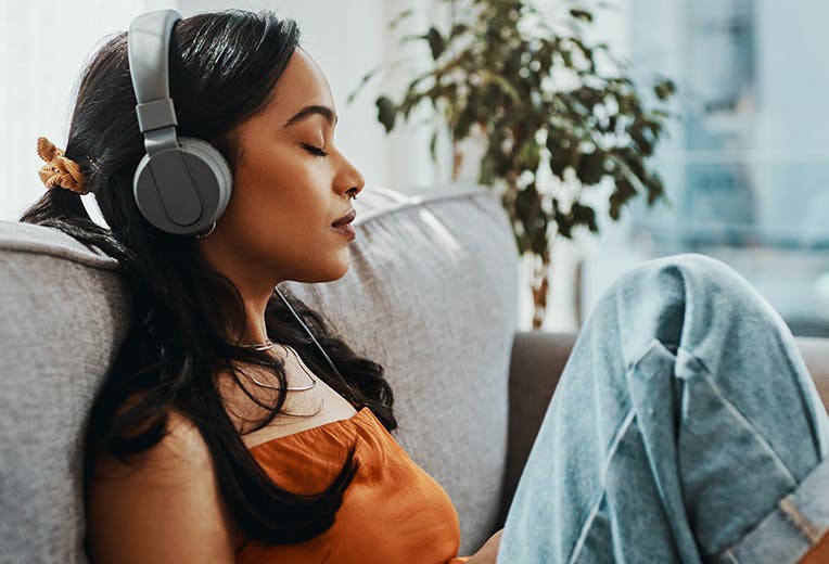 A woman closing her eyes and listening to headphones while sitting on the couch