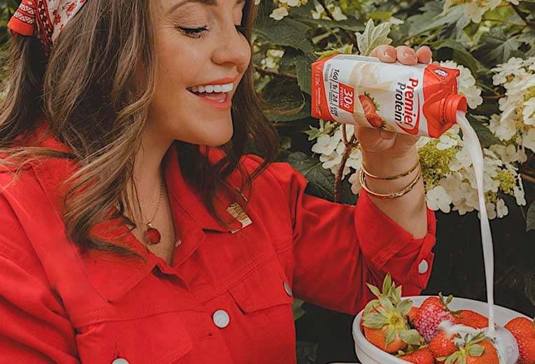 A woman pouring Premier Protein onto strawberries.