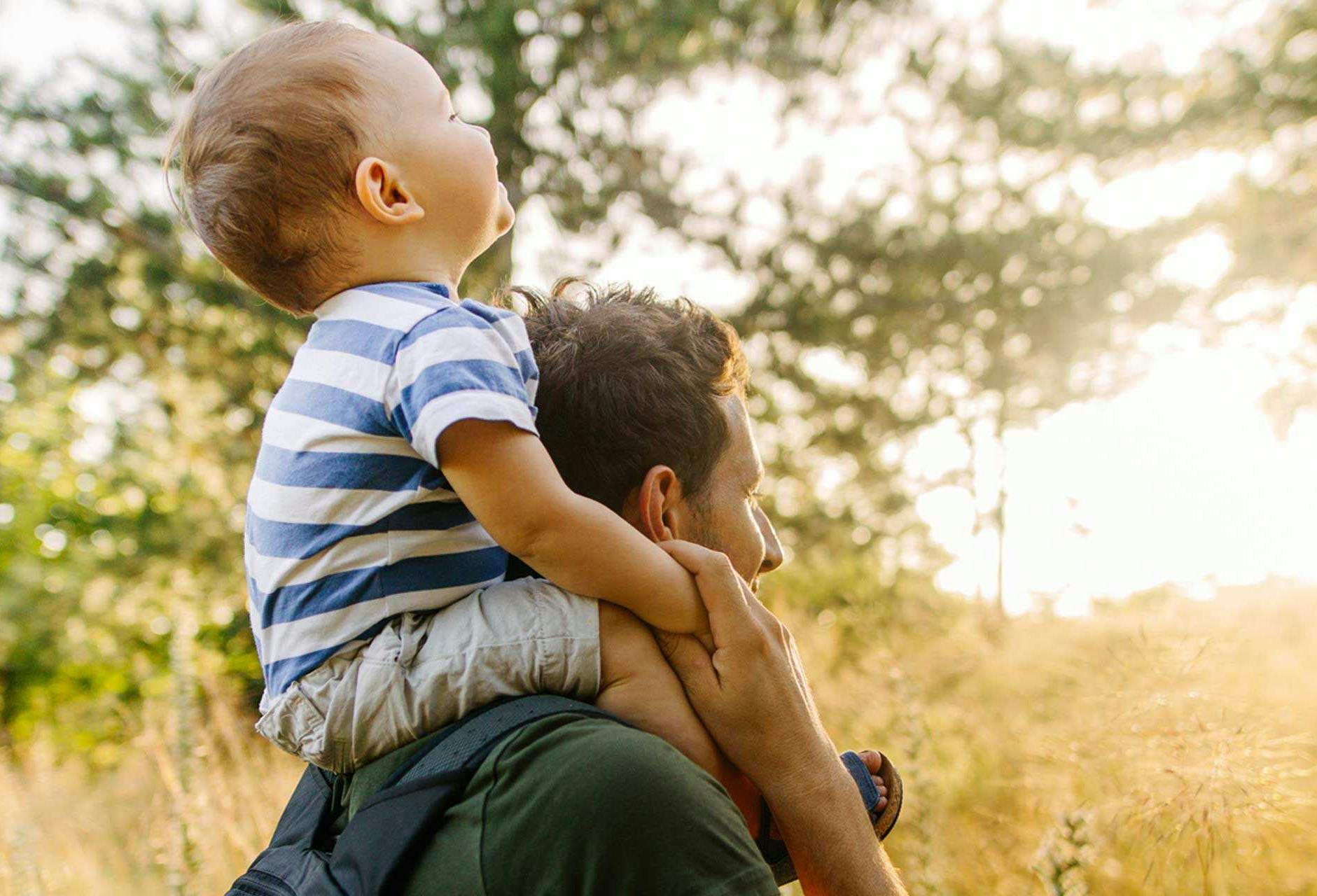 A father walking in the woods with his son on his shoulders.