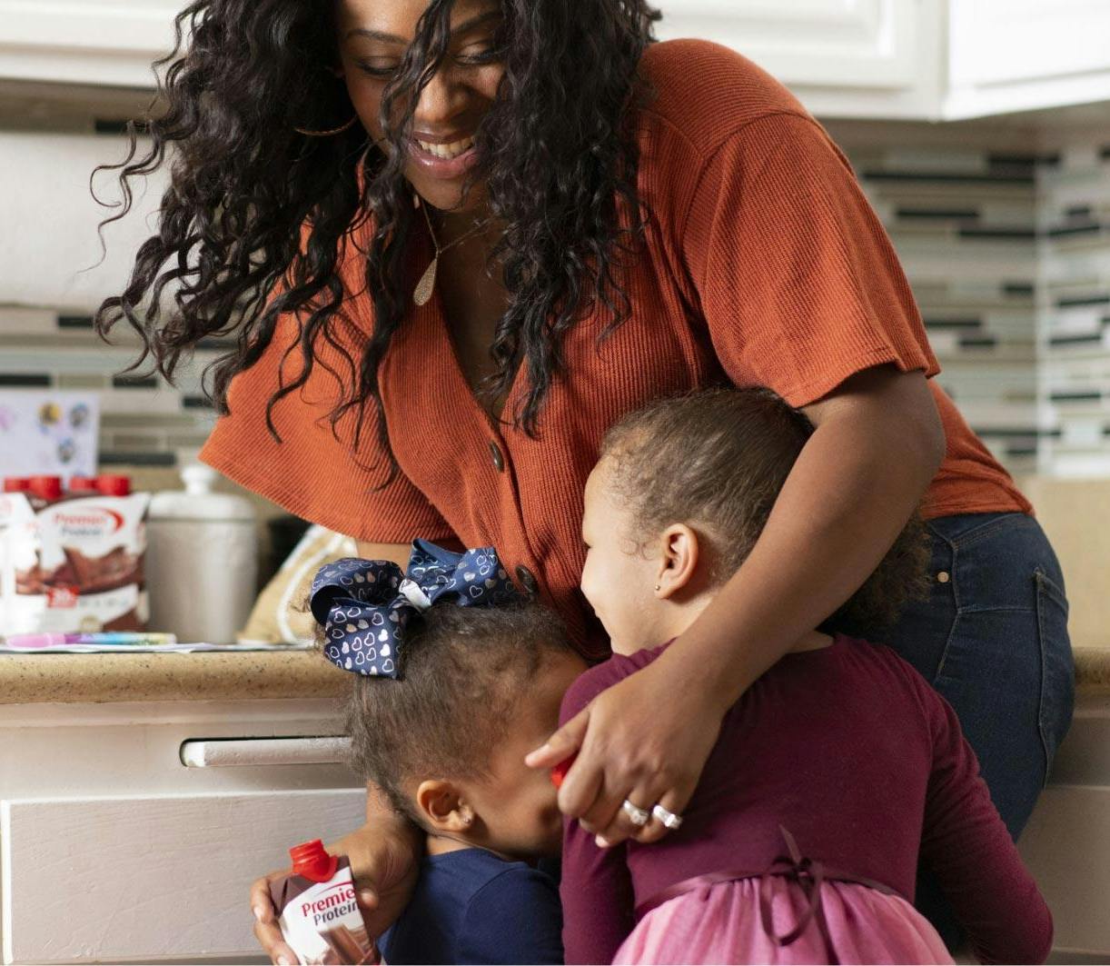 A women hugging her active kids while in her kitchen.