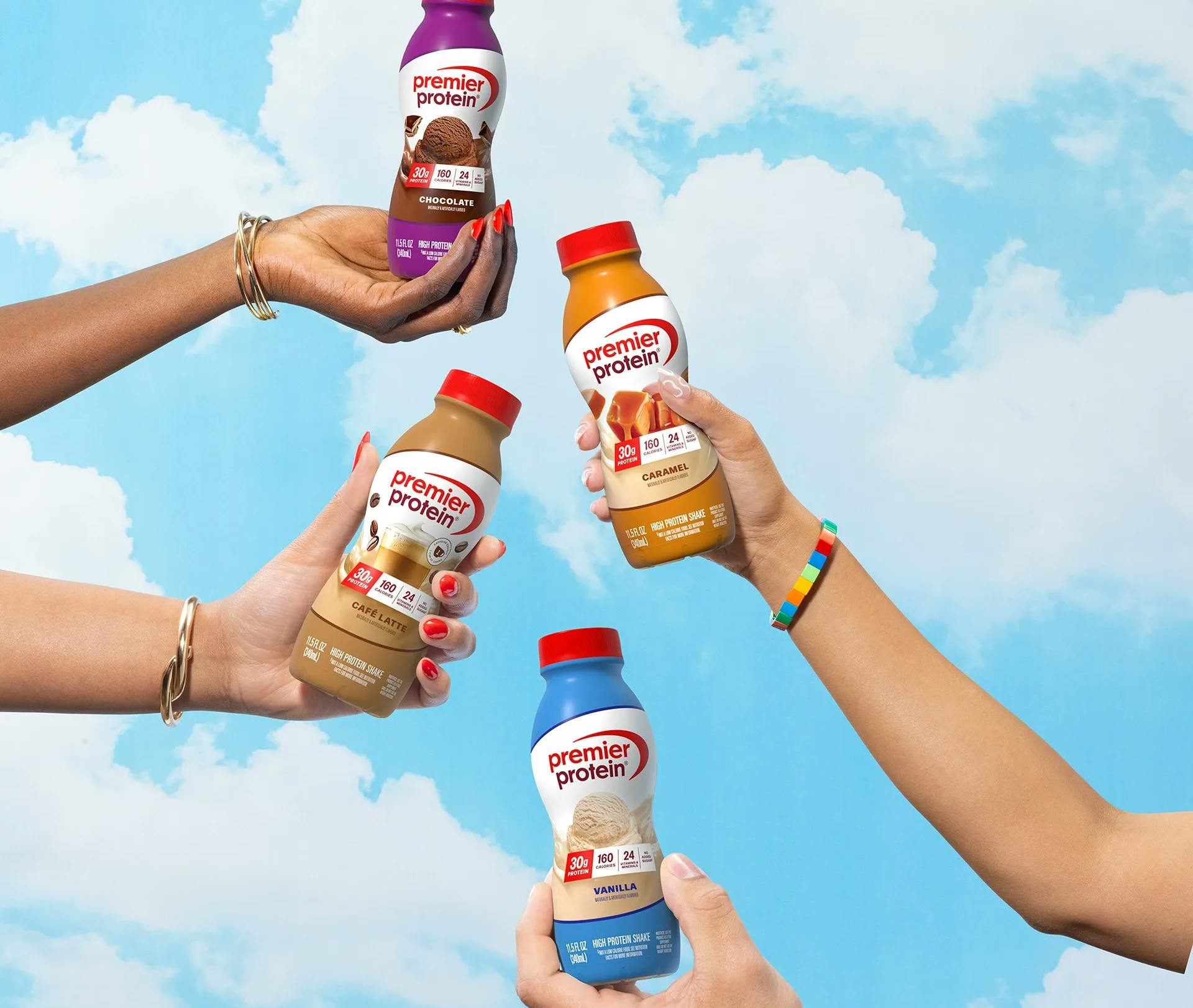Four hands holding Premier Protein shakes in chocolate, caramel, café latte, and vanilla flavors.
