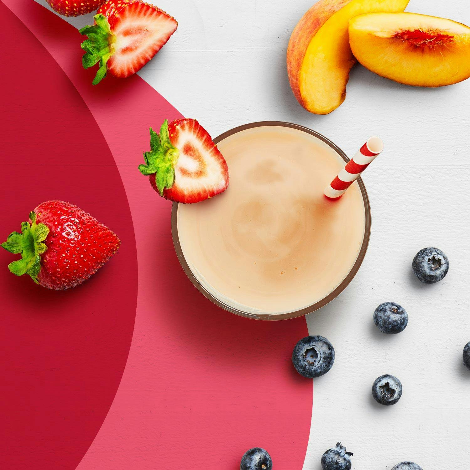 A strawberries and cream Premier Protein shake next to strawberries, peaches and blueberries.