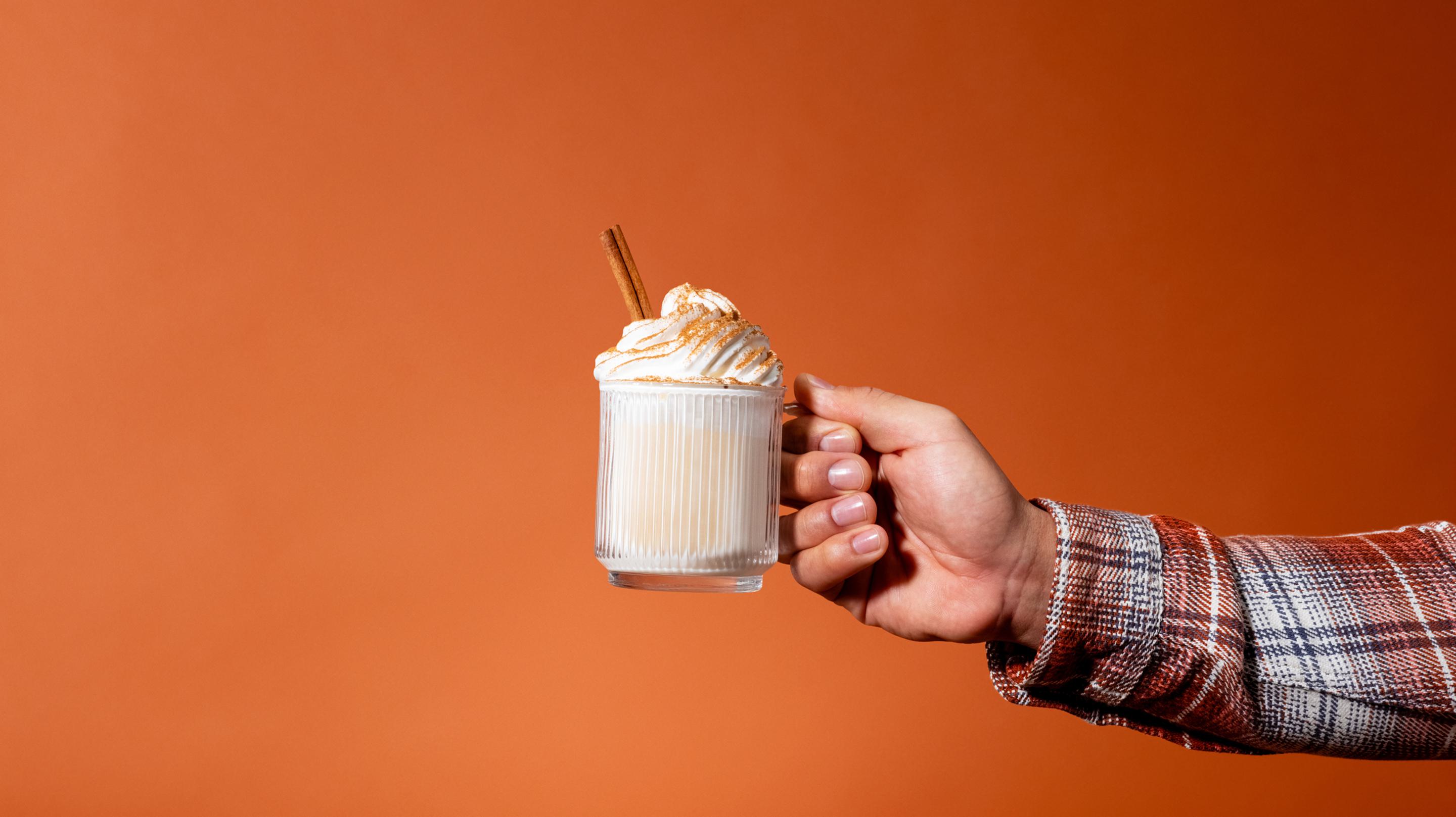 A hand holding a mug with a pumpkin spice protein shake topped with whipped cream and cinnamon.