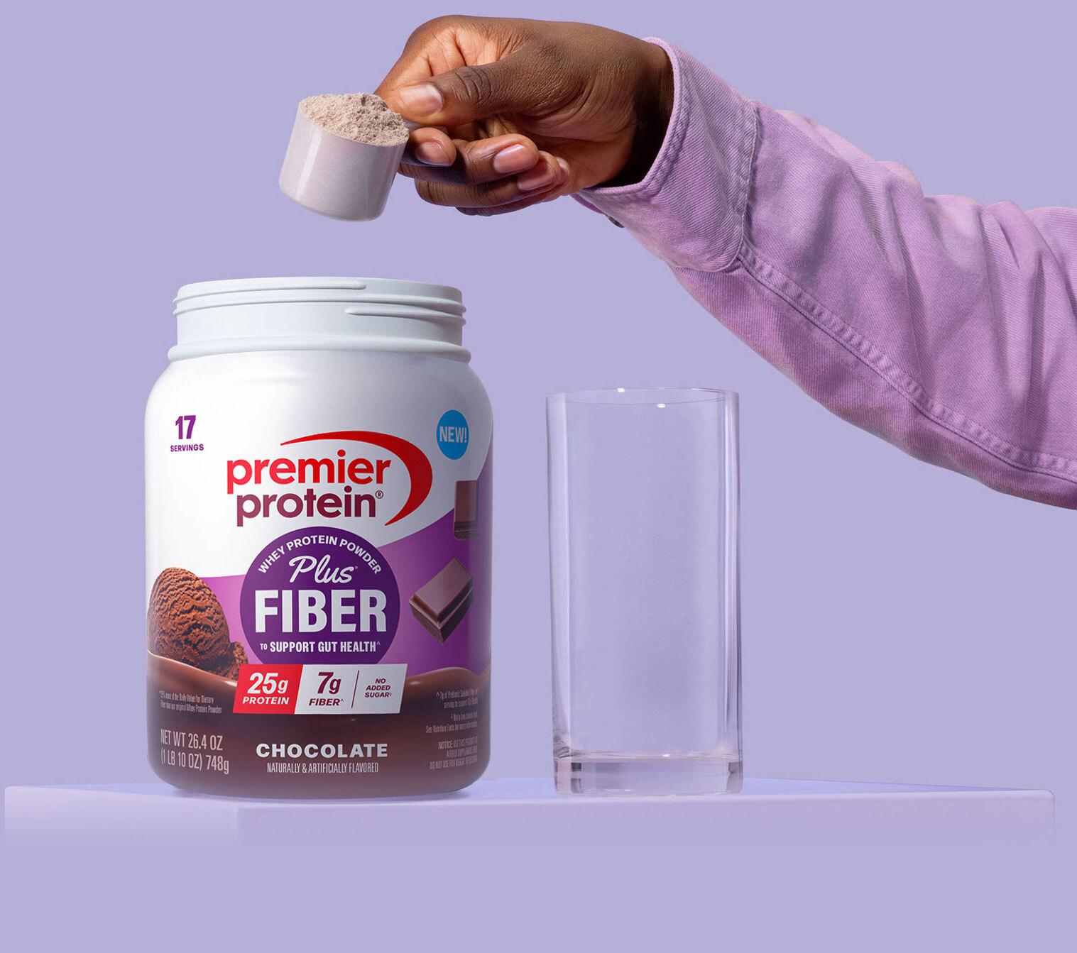 An arm scooping Premier Protein Plus Fiber Powder into a glass